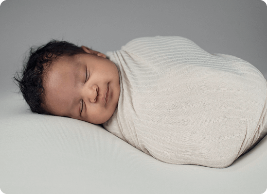 A newborn baby is peacefully sleeping, swaddled in a soft, light-colored blanket against a plain, neutral background—capturing the gentle beginnings celebrated at Grow With Me Pediatrics.