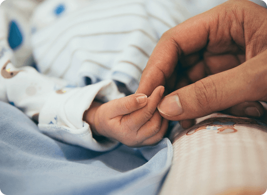 An adult hand gently holding a newborn baby's hand, with the baby dressed in light blue striped clothing—capturing a tender moment that embodies the care and support at Grow With Me Pediatrics.