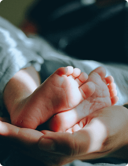 Close-up of an adult hand gently cradling the tiny feet of a baby, softly illuminated by natural light—a heartwarming moment that embodies the nurturing care at Grow With Me Pediatrics.