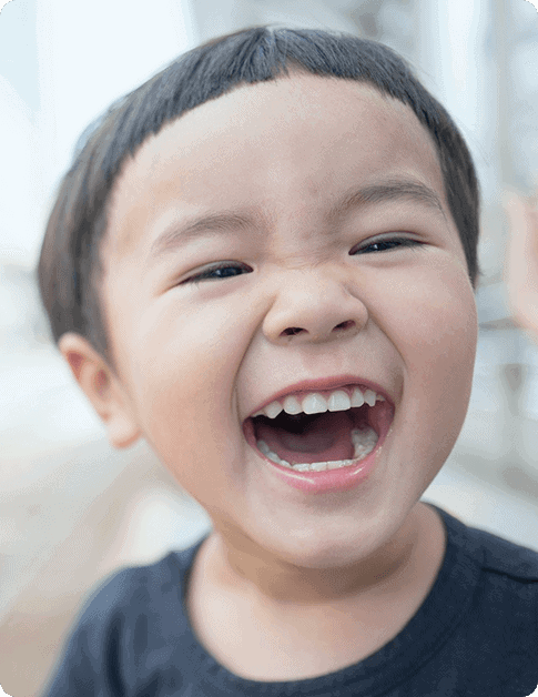 A young child with short, dark hair and a dark shirt is smiling widely, showing teeth and looking directly at the camera—capturing the joyful spirit seen at Grow With Me Pediatrics.