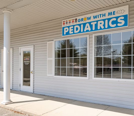 Exterior of a pediatric clinic named "Grow With Me Pediatrics," featuring large windows and a sign above the entrance.
